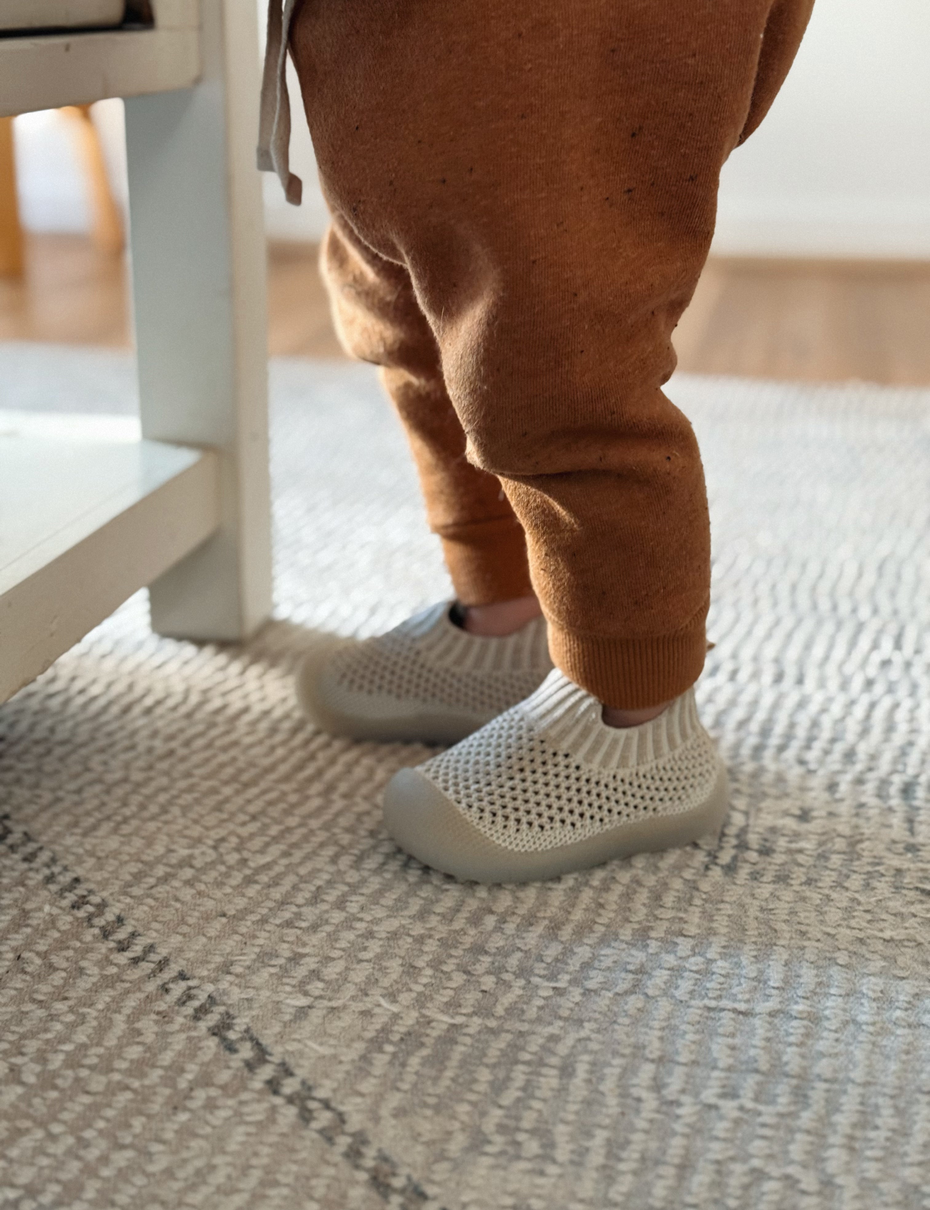 Child's legs wearing brown pants and white socks on a textured floor.
