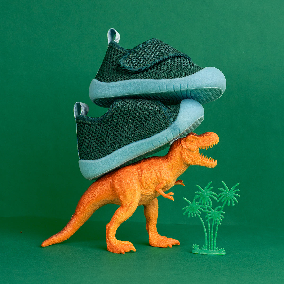Green sneakers stacked on top of a toy dinosaur 